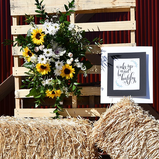 floral spray displayed on wooden pallet with hay bale